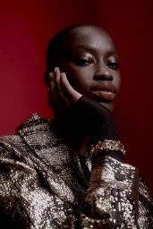 Close-up portrait of a Black woman wearing a metallic gold jacket against a deep red background for Animale.