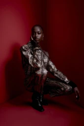 Model crouching in metallic textured pantsuit against a deep red studio background