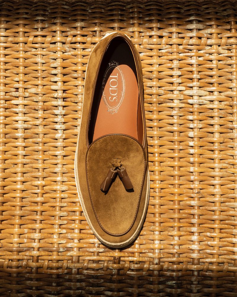 Brown suede Tod's loafer with tassels on woven background in a high-angle shot. The luxury footwear is fashionably displayed.