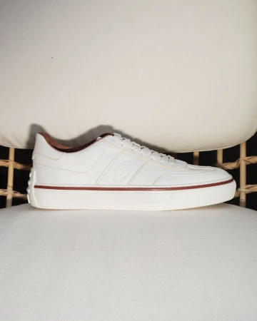 A white leather sneaker with brown trim resting on a white upholstered chair.