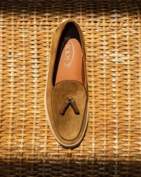 Top down view of a brown suede tassel loafer resting on a woven wicker textured background for Tod's SS24 Men.