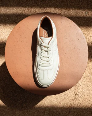White leather sneaker with brown trim resting on a round terracotta pedestal from above