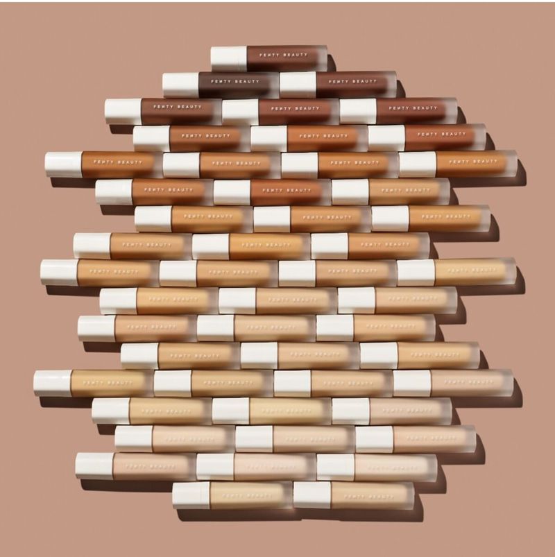 Arrangement of Fenty Beauty concealers in a gradient of shades, showcasing a variety of skin tones on a neutral background.