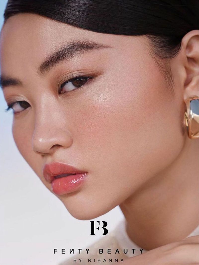Close-up beauty shot of an Asian woman showcasing makeup and wearing gold earrings in a bright, soft light against a blurred backdrop.