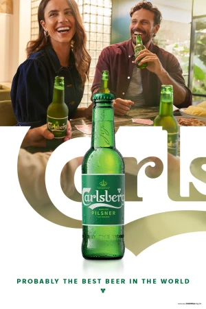Two smiling adults drink Carlsberg beer at a table indoors, with a full bottle in the foreground highlighting the Carlsberg brand.