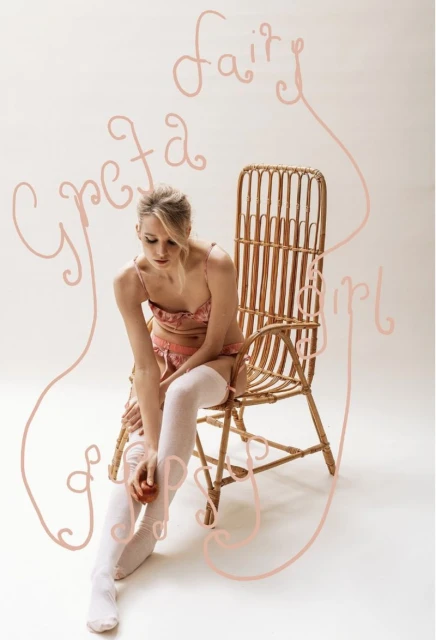 Blonde woman in lingerie sits on a cane chair holding a peach in a studio setting with artistic text effects, creating a dreamy aesthetic.