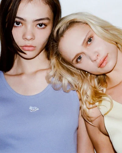 Close-up portrait of two female models posing closely together wearing a blue tank top and yellow tank top against a plain white background.