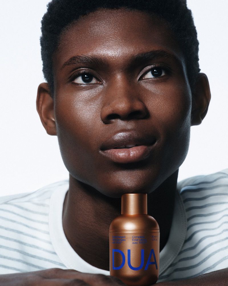 Close-up studio shot of a Black male model with a bronze perfume bottle. Portrait highlights skin, against a plain white backdrop.