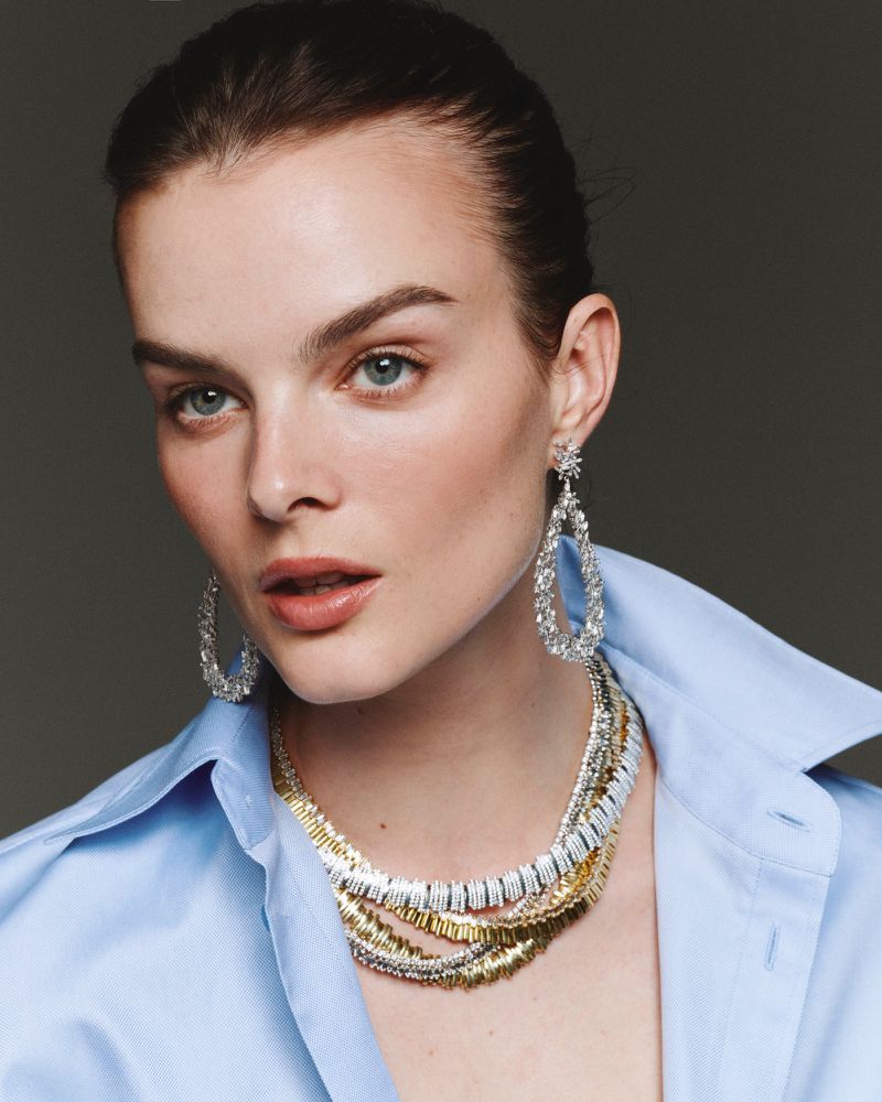 Close-up portrait of model Aylah Peterson wearing layered diamond necklaces and teardrop earrings with a blue shirt for Net-A-Porter.