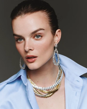 Close-up portrait of model Aylah Peterson wearing layered diamond necklaces and teardrop earrings with a blue shirt for Net-A-Porter.