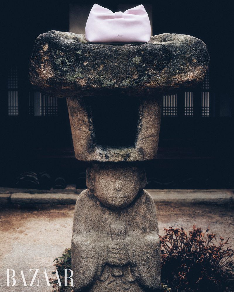Stone lantern with a pink pouch on top, set in a Japanese-style garden, creates a serene and contemplative mood in soft light.