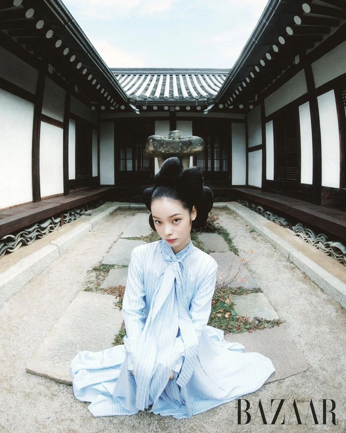 Model with elaborate updo hairstyle wearing light blue striped dress seated in traditional courtyard