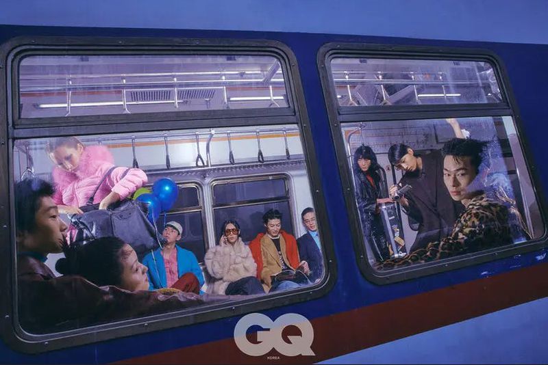 A group of diverse people inside a subway train, captured at eye-level, promoting GQ Korea magazine with dark blue, red, and white colors.