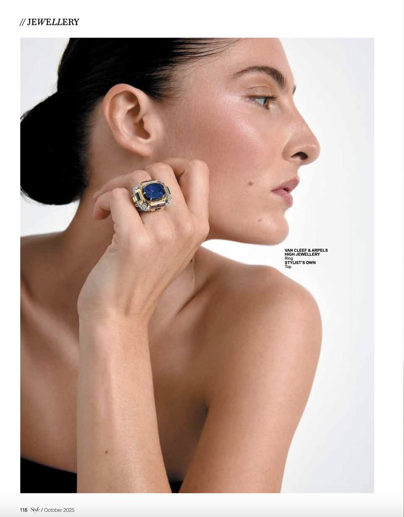 Close-up of adult female model showcasing a large blue gemstone ring with a neutral expression against a bright, light-filled backdrop.
