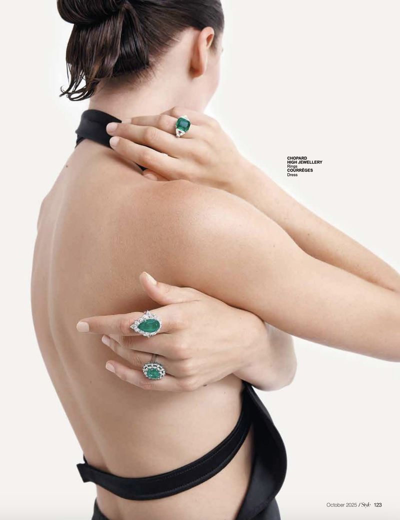 Woman showcases emerald and diamond rings. Black halter top is visible. Jewelry and luxury fashion photography.