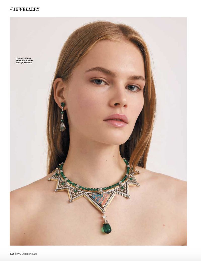 Close-up of a blonde woman modeling high jewelry earrings and a statement necklace featuring green and clear gemstones.