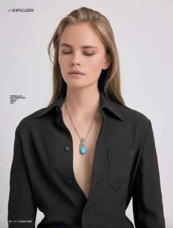 A woman with light brown hair wears a black open button-down shirt and a necklace with a large turquoise pendant against a white background.