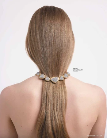 Back view of a woman with long brown hair wearing a triangle-shaped gold and diamond necklace against a clean white background.