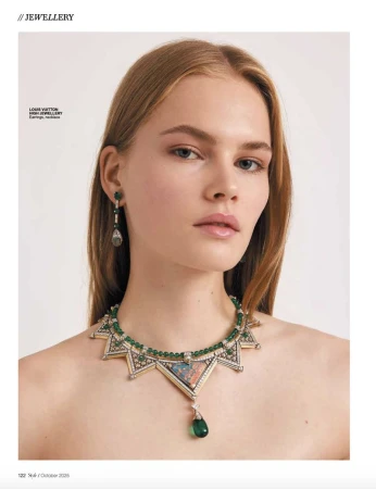 Close-up portrait of a woman wearing an intricate diamond and emerald necklace and matching drop earrings against a plain background