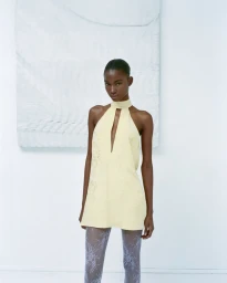 Model in a pale yellow halter dress and patterned tights standing against a white studio background for Maison Sel Lookbook