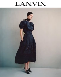 Model in black dress with puff sleeves and black headscarf standing against a neutral studio backdrop for Lanvin