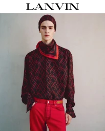 Model wearing a matching patterned black and red silk shirt and cap with bright red trousers against a grey seamless background