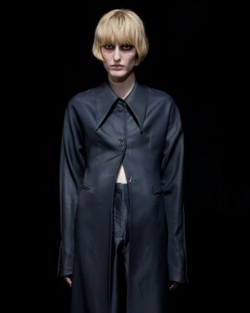 Model with blonde bob wearing a dark buttoned coat against a black background for Grace Ling S/S 26