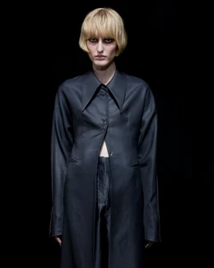 Model with blonde bob wearing a dark buttoned coat against a black background for Grace Ling S/S 26