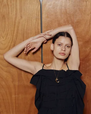 Model posing against a wood paneled wall wearing a black ruffle top and gold necklace for Eudon Choi SS24 campaign