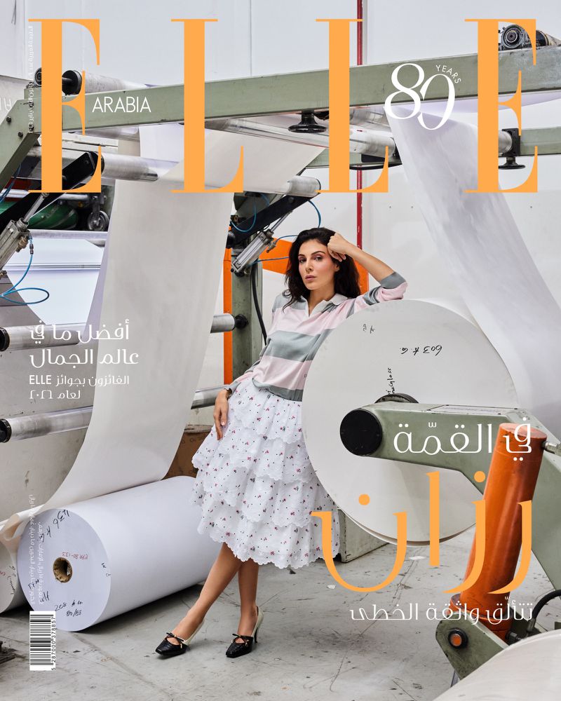 Elle Arabia magazine cover featuring a brunette woman in a floral skirt posing next to a paper-manufacturing machine, editorial fashion.