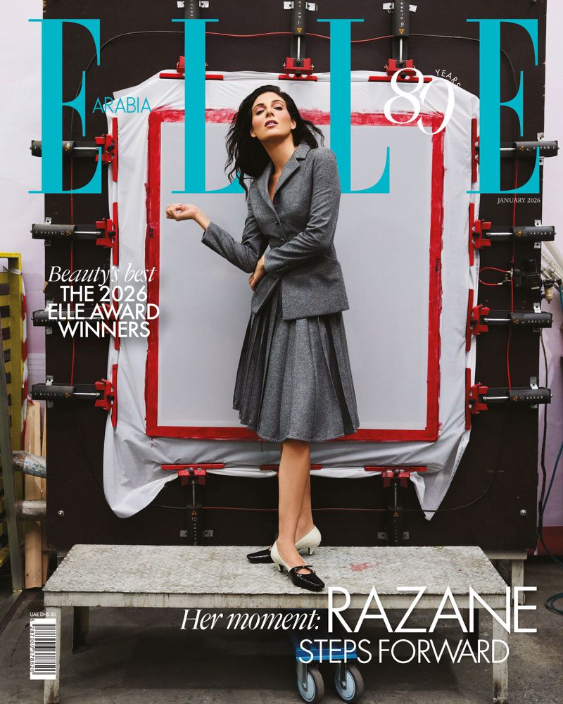 Elle Arabia magazine cover featuring a brunette woman in a grey suit and skirt, posing on a metal platform in front of a prop.