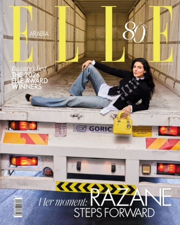 Razane Jammal reclining on the back of a cargo truck wearing a black military jacket and flared jeans for Elle Arabia cover.