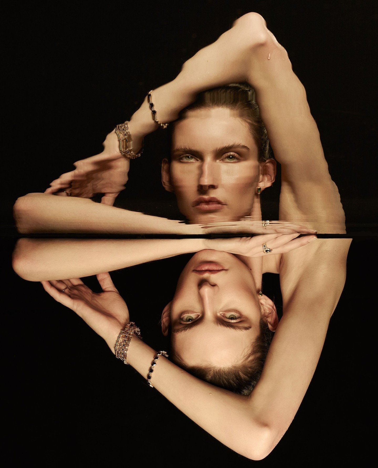 Model with bracelets reflected in water against a dark background for Temple of the Sun Reflections campaign