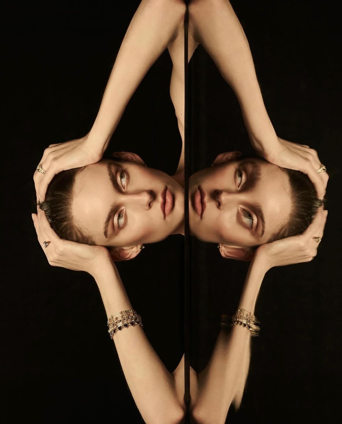 Model with stacked bracelets and rings framed in a mirror reflection against black background for Temple of the Sun