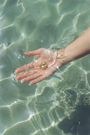 Close-up shot of a person's hand in water, holding a small golden nugget against a clear, turquoise water background.