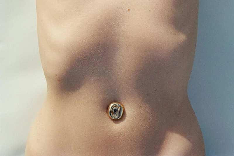 Closeup studio shot of a fair-skinned human torso with shadows, and a gold and black decorative button over the navel.