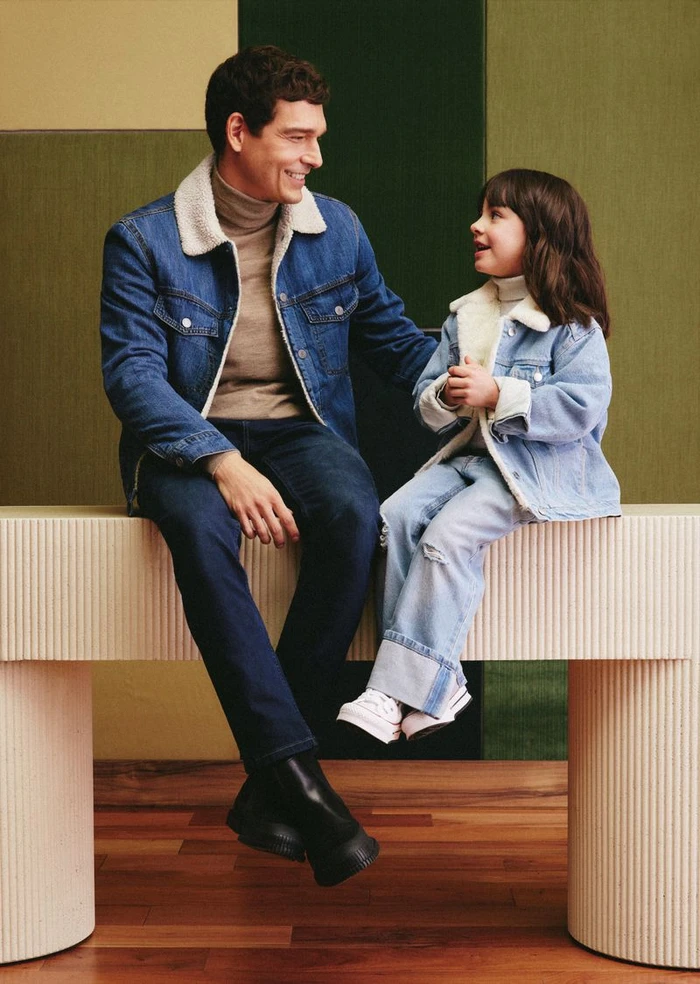 Man and child seated on a structured bench wearing matching denim jackets with white fleece collars for Falabella Father's Day 2024