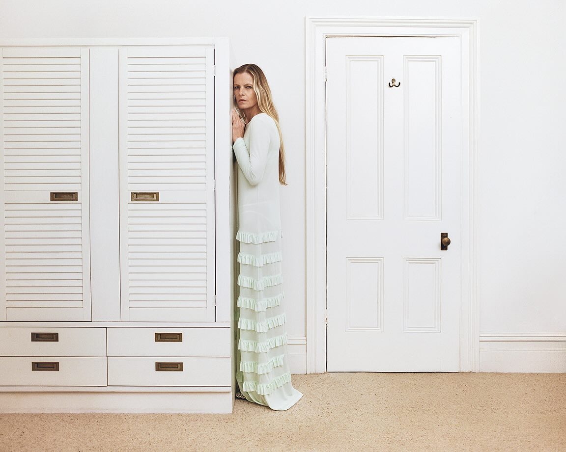 Adult female in a light green gown standing between a white wardrobe and white door inside a room with light walls and carpet.