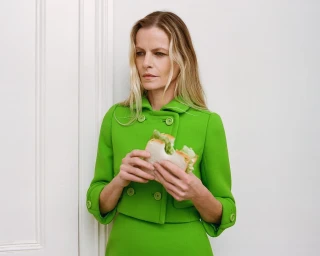 Woman wearing a bright green jacket holding a sandwich against a white paneled door background.
