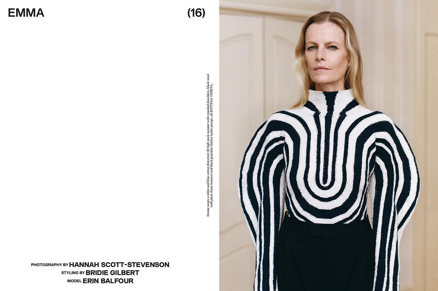 Portrait of a blonde woman wearing a black and white striped knit sweater with a high neck and long sleeves against a neutral wall.