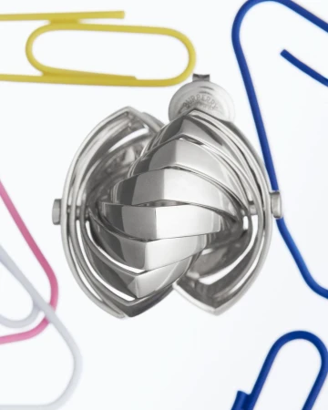 Close-up of a silver sphere with geometric patterns surrounded by colorful paper clips on a white background with studio lighting.
