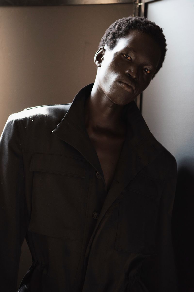 Close-up studio shot of a Black man with dark curly hair wearing a dark button-up shirt, looking at the camera with neutral expression.