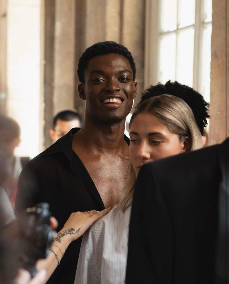 Close-up of an African American man smiling next to a blonde woman in an indoor setting with a blurred group of people in background.