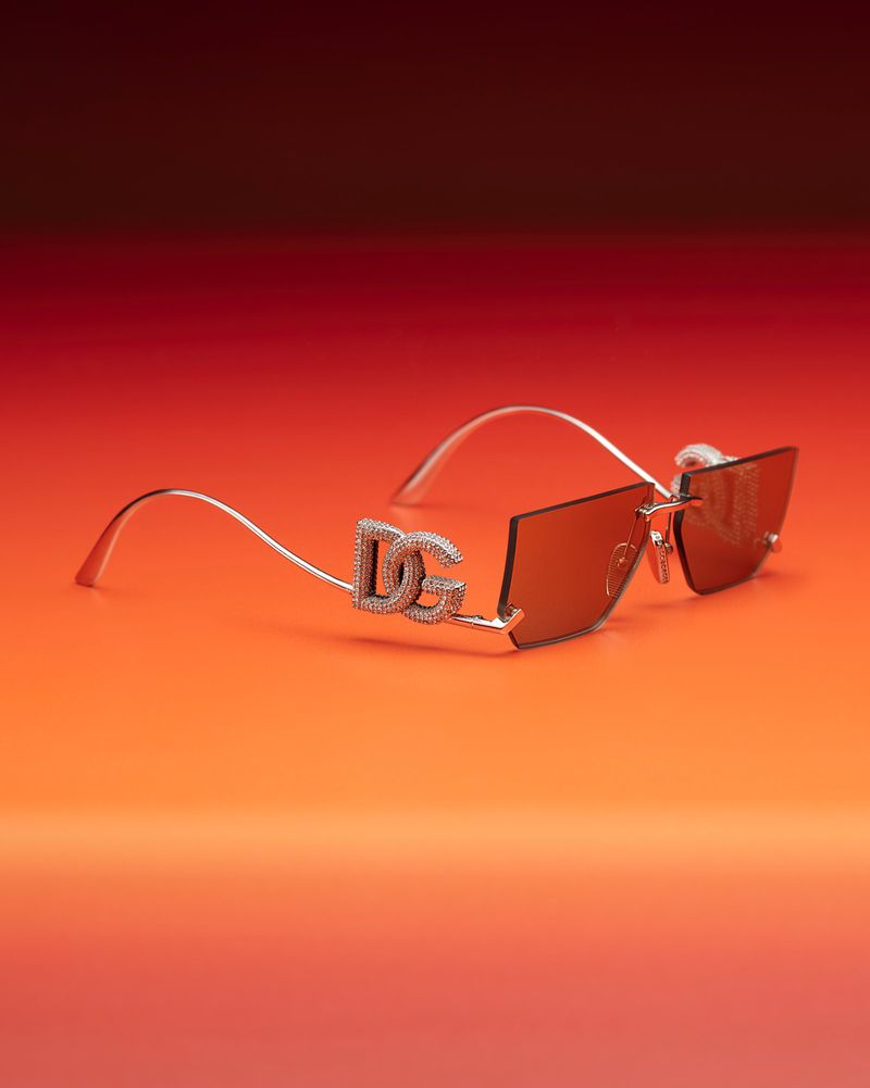 Close-up of Dolce & Gabbana sunglasses with crystal accents on a gradient orange and red background. Fashionable eyewear detail shot.