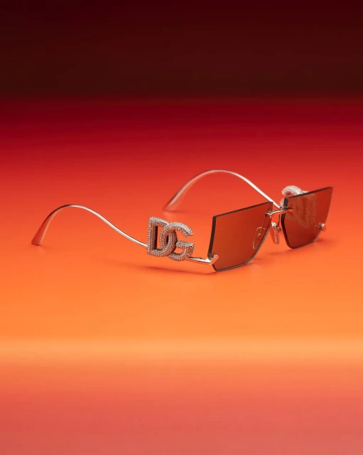 Close-up of Dolce & Gabbana sunglasses with crystal accents on a gradient orange and red background. Fashionable eyewear detail shot.