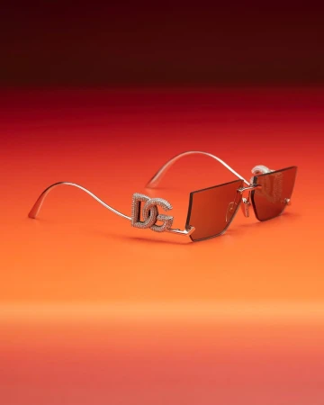 Close-up of Dolce & Gabbana sunglasses with crystal accents on a gradient orange and red background. Fashionable eyewear detail shot.