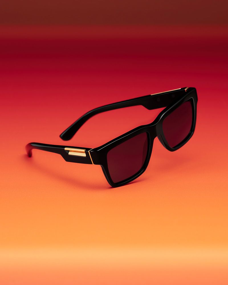 Studio shot of black-framed sunglasses with red lenses on an orange and red gradient background, product photography, eyewear.