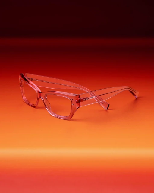 Pink-tinted glasses on a gradient background transitioning from warm orange to deep burgundy. Product shot highlights frame details.