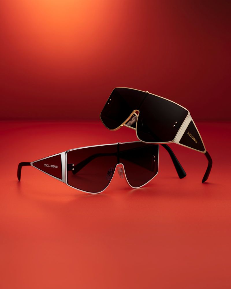 Two pairs of Dolce and Gabbana sunglasses are displayed against a vibrant red backdrop in a fashion product shot.
