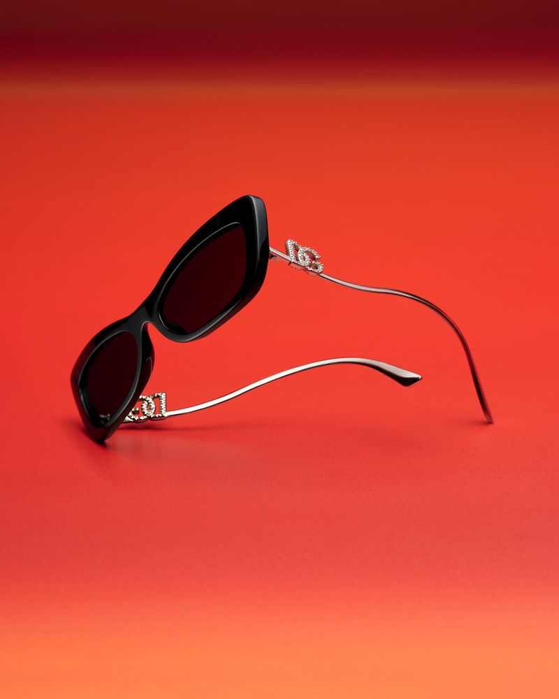 Angular black sunglasses with silver arms on a gradient red background. Close-up product shot for fashion accessories and eyewear.